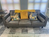 Front view of charcoal leather sofa with cushions and blanket