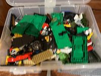 View inside the open plastic bin showing a variety of LEGO bricks in colors green, red, black, tan, and yellow among others.