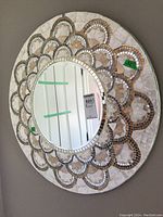 Side angled view showing the circular mosaic wall mirror hanging on a gray wall; mirror and frame details visible.