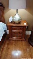 Full view of walnut nightstand with lamp and a decorative plate on top.