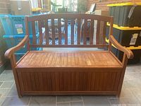 Front view of a wooden outdoor storage bench showing slatted seat, backrest, and armrests.