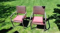 Two brown wicker style patio chairs with metal frames and red cushioned seat pads on grass outdoors.