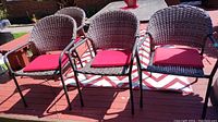 Four faux wicker patio chairs with red cushions on a wooden deck in outdoor setting.