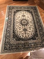 Full view of the rectangular area rug on a hardwood floor showing the overall black and cream floral pattern and size.