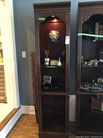 Front view of the tall wood shelving unit showing crown molding, shelves with decorative items, and closed base compartment.