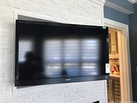Front view of Sony TV mounted on white textured wall, screen off, reflections visible.