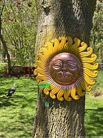 Metal sun wall decoration with curled rays and face in center, attached to tree