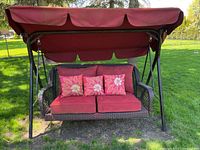 Front view of the wicker swing showing seat cushions, three floral-patterned pillows, and the red canopy above.