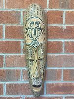 Front view of first wooden mask showcasing carved facial features and painted tribal faces on top.