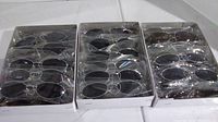 Tray containing multiple pairs of sunglasses individually wrapped, showing silver and bronze tone frames