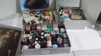 Three metal tins filled with an assortment of sewing thread spools of various colors and sizes shown in perspective angle.