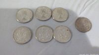 Seven silver Canadian fifty cent coins laid out on a white cloth, showing obverse and reverse sides. Coins date from 1963, 1964, and 1965, showing signs of wear and tarnish.