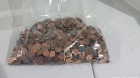 Plastic bag containing a large quantity of mixed US and Canadian pennies with visible different aging and wear.