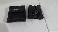 Olympus binoculars next to soft fabric carrying case, both on a white surface.