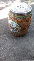 Side view of the ceramic garden stool showing the yellow lattice pattern with a large oval floral motif and bird design.