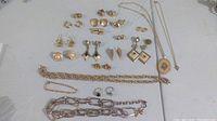 Photo showing variety of 14 pairs of gold tone earrings, 4 necklaces with pendants, 1 bracelet and 2 rings arranged on flat surface