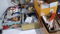 Overview of sewing supplies organized in five tins and one box, showing a variety of sewing tools and thread spools.