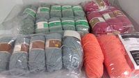 View showing multiple yarn skeins in green, burgundy, blue, and orange colors packaged in plastic wrapping and loose