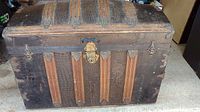 Front and top side view of vintage wooden domed trunk with leather and metal detailing, highlighting lock area and overall condition.