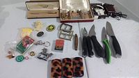 Three pairs of folding cheater glasses with tortoiseshell cases and multiple tools including folding knives, lighter, cufflinks, and pen box