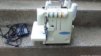 Front view of white Reliable serger with four thread spools on concrete step