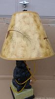 Full side view of the lamp showing the tapered lampshade with pine needle design and the black bear figurine base with visible power cord wrapped around it.