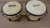 Top and angled view of two Rock Jam natural wood bongos with black metal tuning hardware and natural skin drumheads.