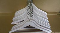 Stack of 20 white wooden hangers laid flat showing metal swivel hooks arranged together.