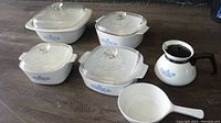Photo of all six items arranged on floor: four square Corning Ware Blue Cornflower casseroles with glass lids, one white skillet with handle, one white coffee pot with black handle