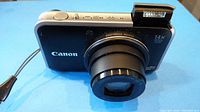 Front angle view of Canon PowerShot SX210 IS digital camera with lens extended and flash raised.