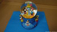 Front view of the Disney Hallmark musical snow globe showing Mickey and Minnie Mouse inside the globe with balloons and surrounding character figures on base.