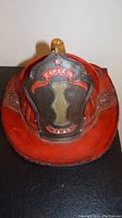 Front view of red leather firefighter helmet with Captain shield and gold eagle on top.