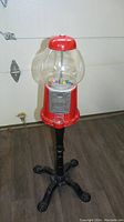 Front view of vintage red gumball machine on black metal stand showing the globe with colorful gumballs inside and coin slot on red metal base.