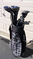 Full view of black and plaid Bennington golf bag with golf clubs inside, showing head covers on fairway woods and hybrids.