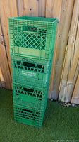 Four green milk crates stacked outside on grass against a wood fence, showing front and side with 'Foremost Dairy Inc.' logo.