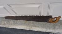 Full view of the vintage hand saw showing the entire blade and handle on a concrete surface.
