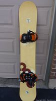 Full view of yellow Nitro Type A snowboard with red and black circular design and black and orange bindings mounted, showing normal wear.