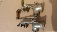 Side view of two vintage manual meat grinders showing metal bodies, wooden handles, hand clamps, and condition