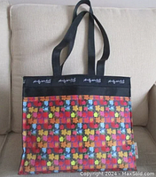 Front view of Andy Warhol floral print tote bag showing colorful flowers on checkered background and black top edge with white signature and straps.