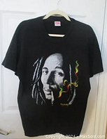 Black t-shirt on hanger showing full Bob Marley graphic and cigarette with Jamaican colored smoke detail.