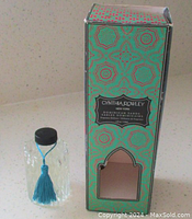 Photo of the glass fragrance diffuser bottle with a black cap and blue tassel beside its turquoise patterned box showing some wear.