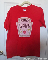 Red Heinz Tomato Ketchup T-shirt hung on a hanger showing the full front view with the ketchup label graphic.