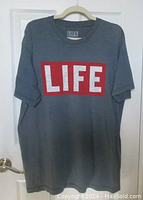 Full front view of the blue-gray LIFE magazine t-shirt hanging on hanger showing logo and overall condition.