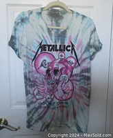 Full front view of the tie dye Metallica t-shirt hanging on a hanger against a white door.
