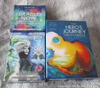 Photo shows three oracle decks: Miracles Now by Gabrielle Bernstein, Advancing Life Oracle by Robert G. Novak, and The Hero's Journey Dream Oracle by Kelly Sullivan Walden and Rassouli enclosed in their original boxes.
