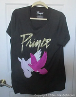 Full front view of grey Prince t-shirt showing large graphic of white and purple doves and metallic gold Prince logo.