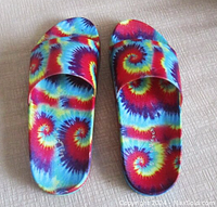 Pair of tie dye psychedelic print slide sandals by Steve Madden laid flat on a beige surface showing top view of the sandals.