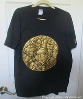 Front view of dark navy blue Versace T-shirt hanging on hanger with large gold metallic Medusa head design on the chest.