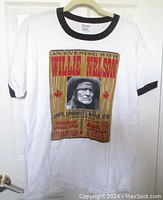 Full front view of white T-shirt with black collar and sleeve trim showing large graphic of Willie Nelson concert poster from 2006 Peterborough event.