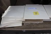 Stack of white square tiles with marble veining, 12x12 inches size, arranged in two piles on a flat surface.